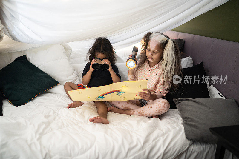 兄弟姐妹们在家里的毛毯帐篷里玩着望远镜和手电筒- - - - - - -一个有花斑的女孩